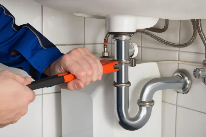 Canalizador a apertar o sifão de um lavatório com uma chave de tubos