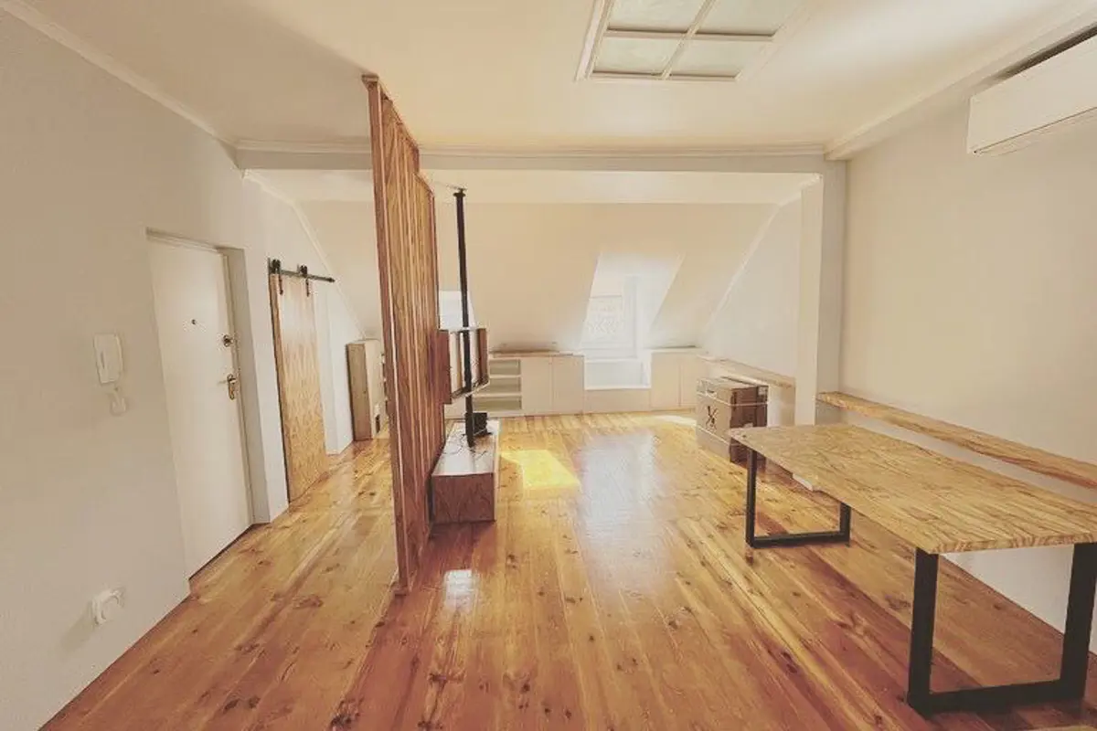 Sala em águas-furtadas com soalho de pinho e porta de correr em madeira, na Calçada de Sant'Ana
