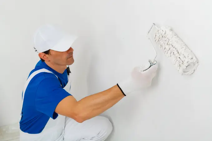Pintor de boné e fato branco a passar o rolo numa parede interior