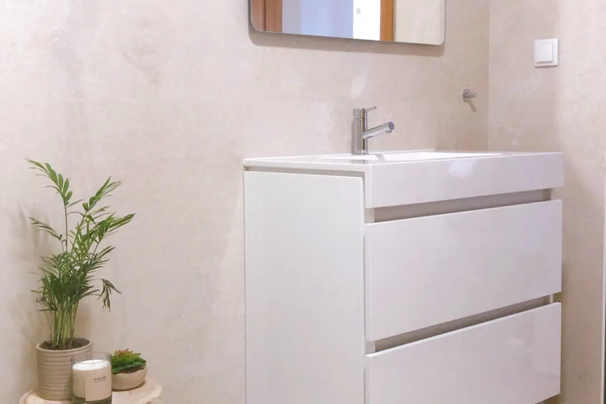 Casa de banho remodelada em tons de areia, com móvel branco suspenso e espelho iluminado