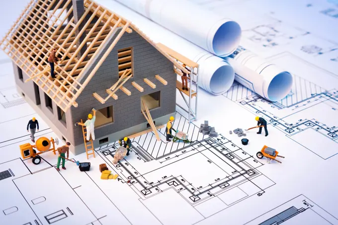 Maqueta de uma casa em construção pousada sobre plantas e rolos de desenho