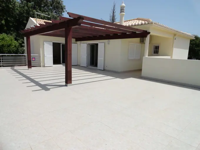 Terraço ladrilhado com pérgula de madeira em frente a uma moradia térrea no Algarve